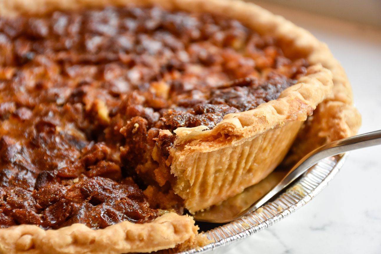 Runder Apfelkuchen mit vielen Nüssen auf einer Tortenplatte.