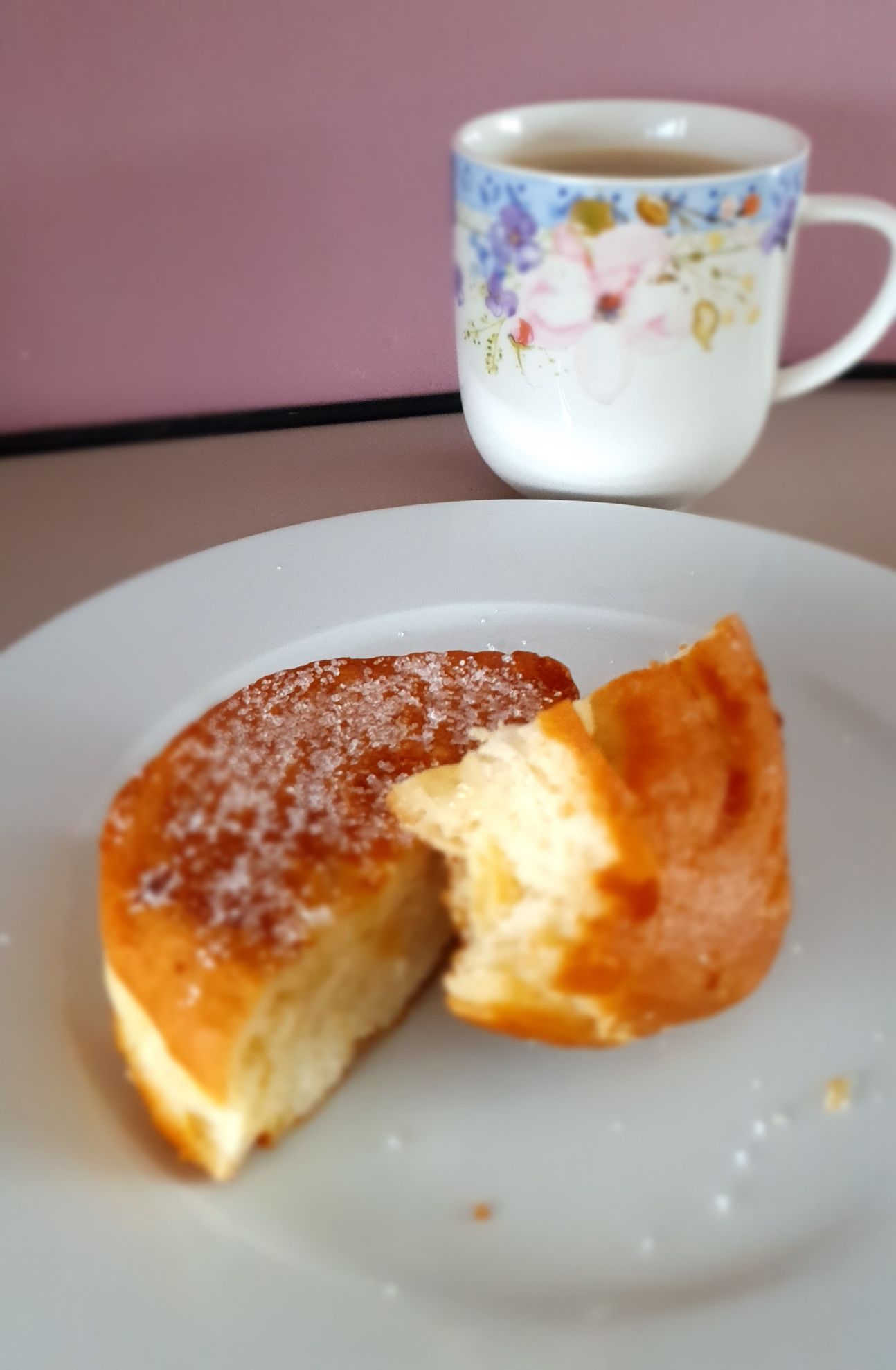 Ein Teller, darauf ein geteilter Apfel-Berliner und eine Tasse im Hintergrund.