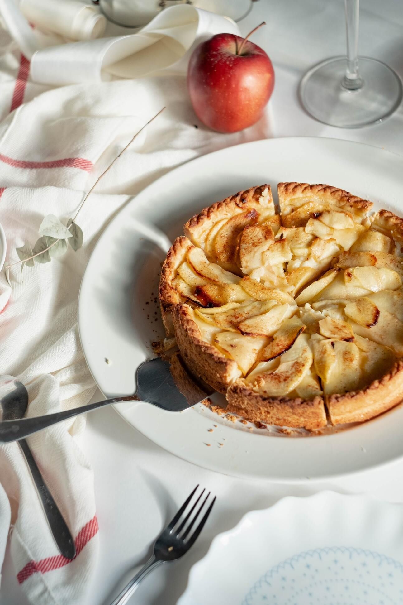 Apfelkuchen auf runder Kuchenplatte, mit einem Apfel dekoriert.