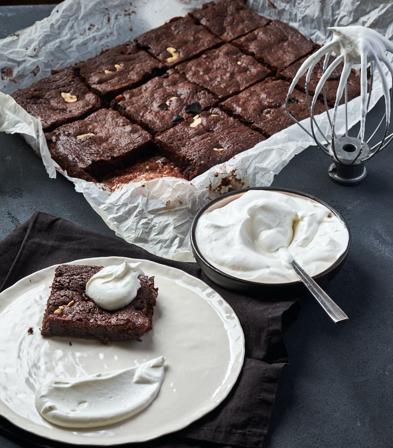 Ein Brownie mit Sahne auf einem Teller angerichtet, im Hintergrund mehrere Brownies.