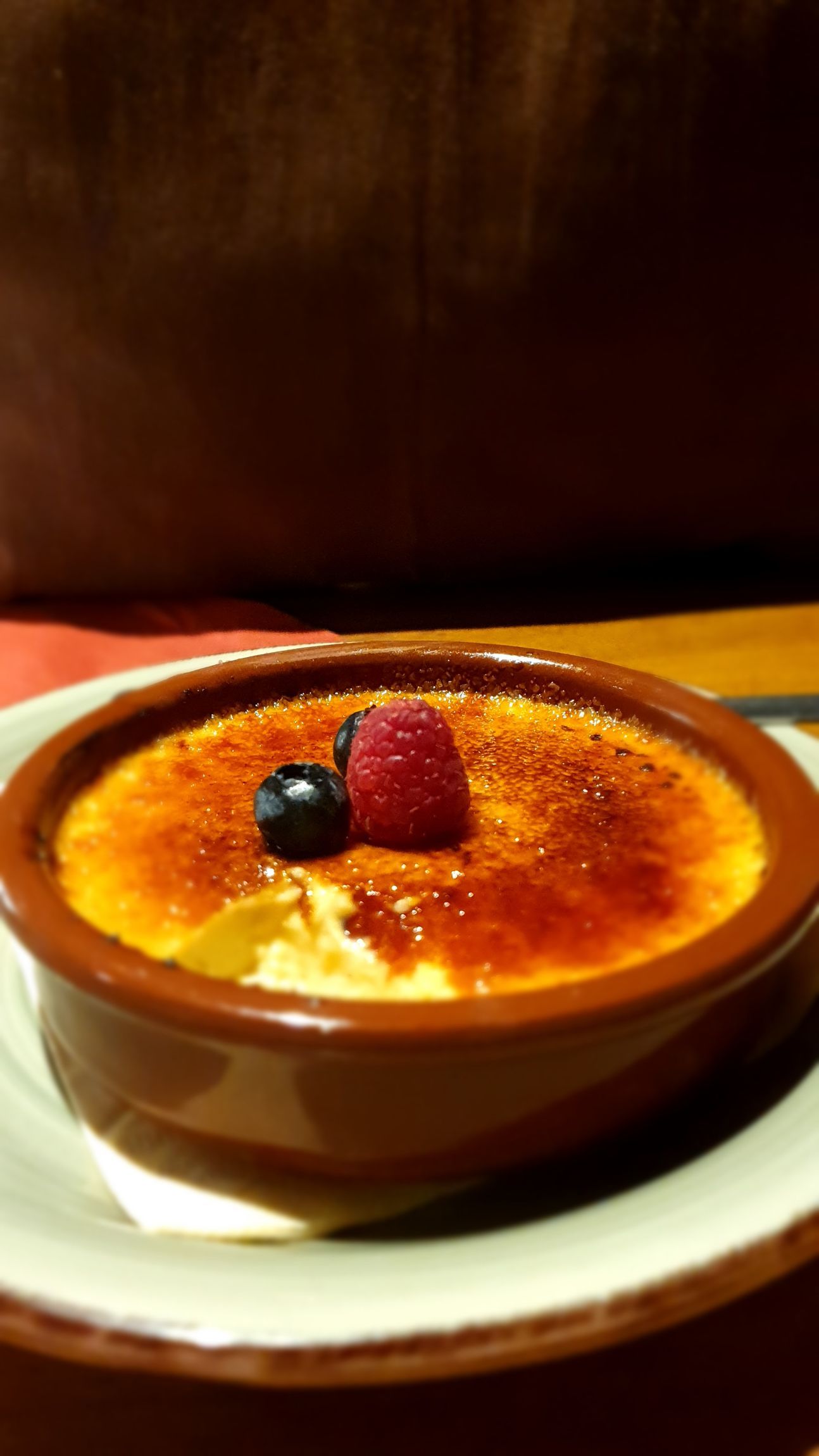 Eine, auf der Oberfläche, karamellisierte Creme in einem braunen, runden Schälchen, mit Beeren dekoriert.