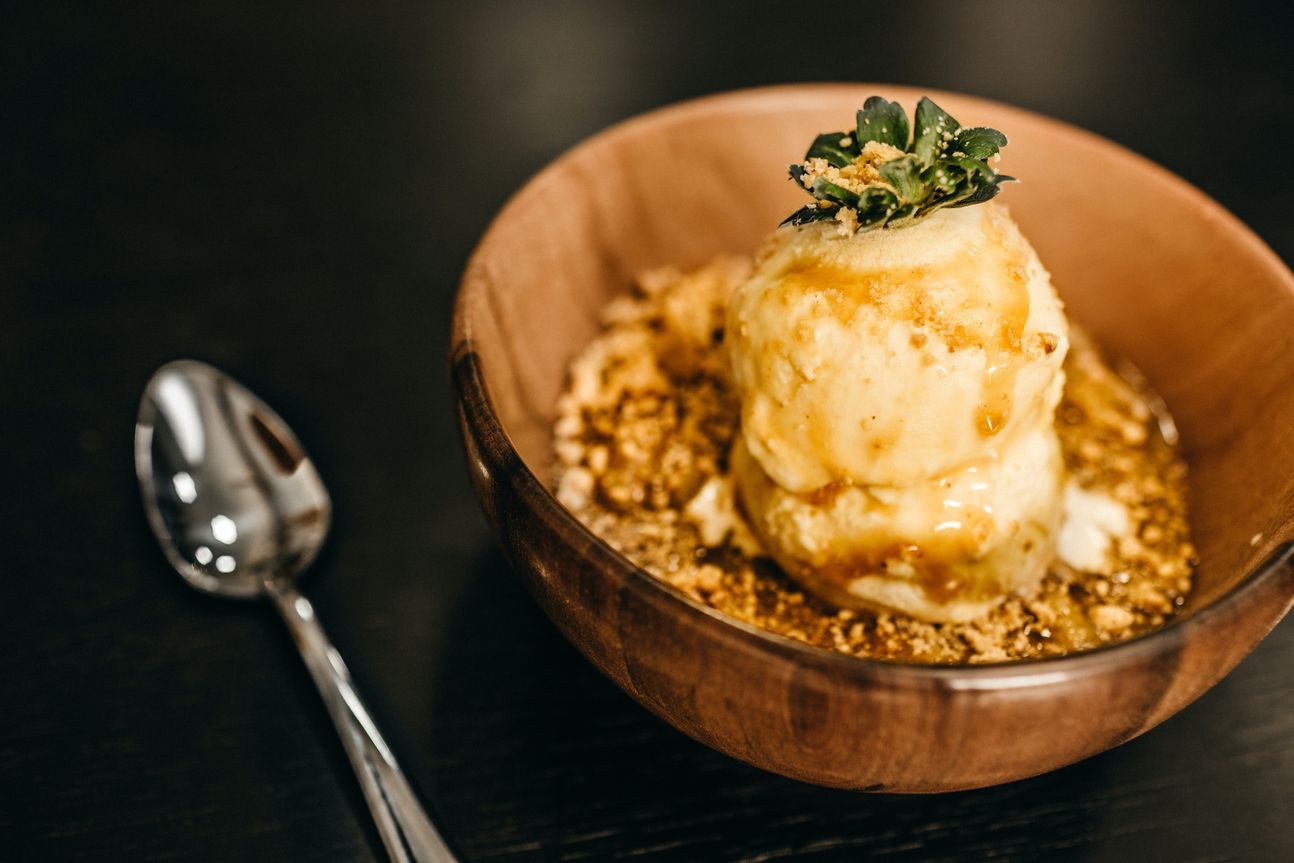 Crumble in einer Holzschale, darauf eine Kugel Eis, links daneben ein Löffel.