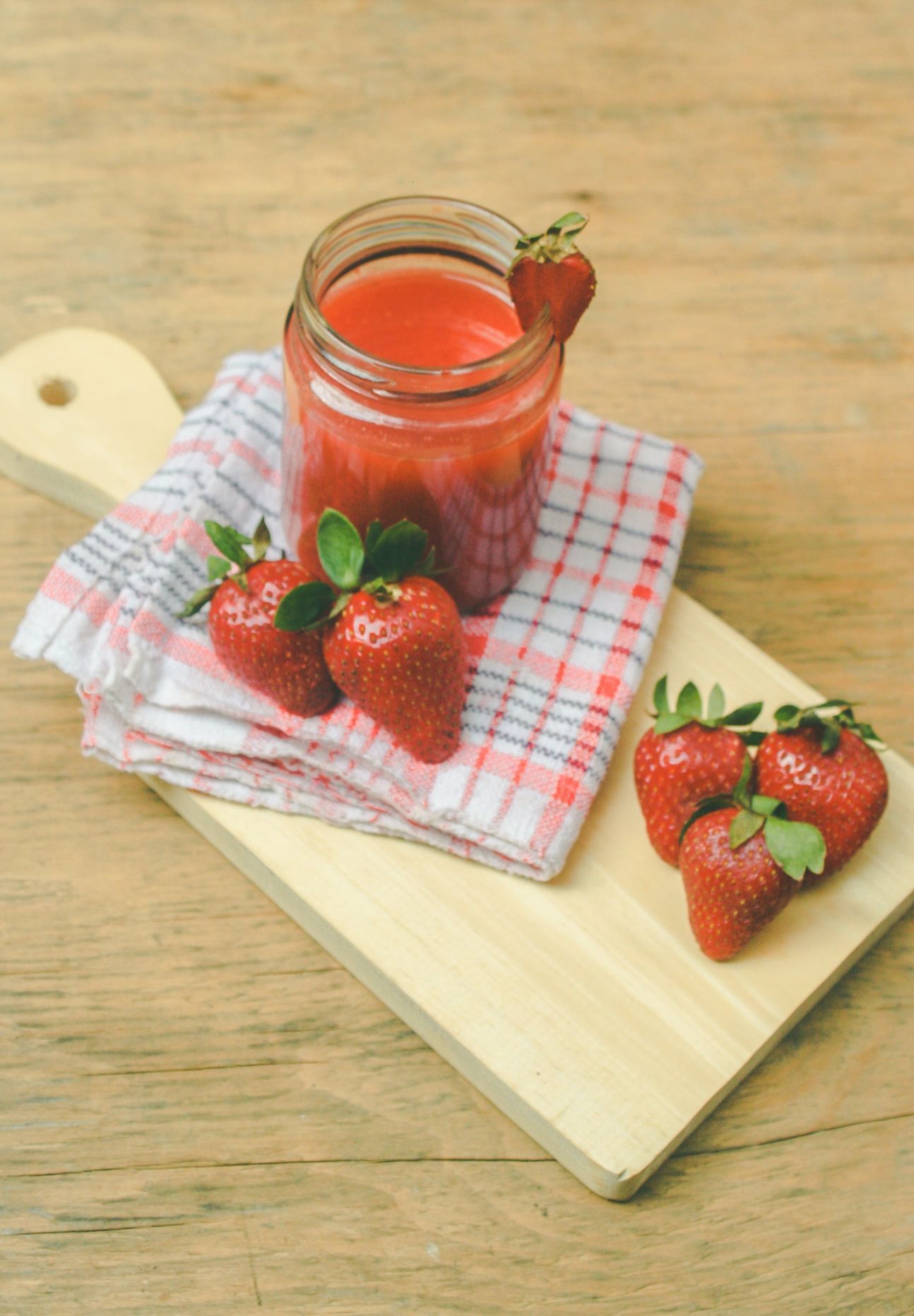 Auf einem Holzbrett eine Serviette. Darauf ein Glas Marmelade, dekoriert mit Erdbeeren.