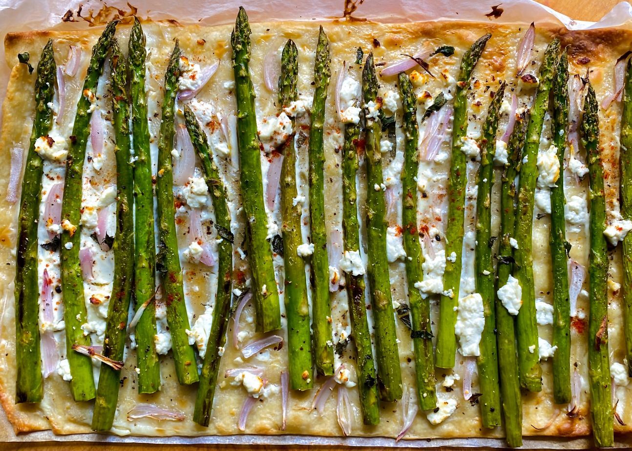 Flammkuchen in der Größe eines Backblechs, belegt mit grünem Spargel.