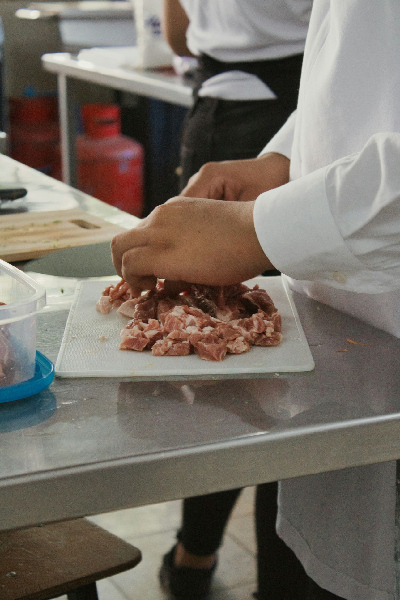 Mehrere Fleischstücke auf einem weißen Teller und zwei Hände, die das Fleisch berühren.