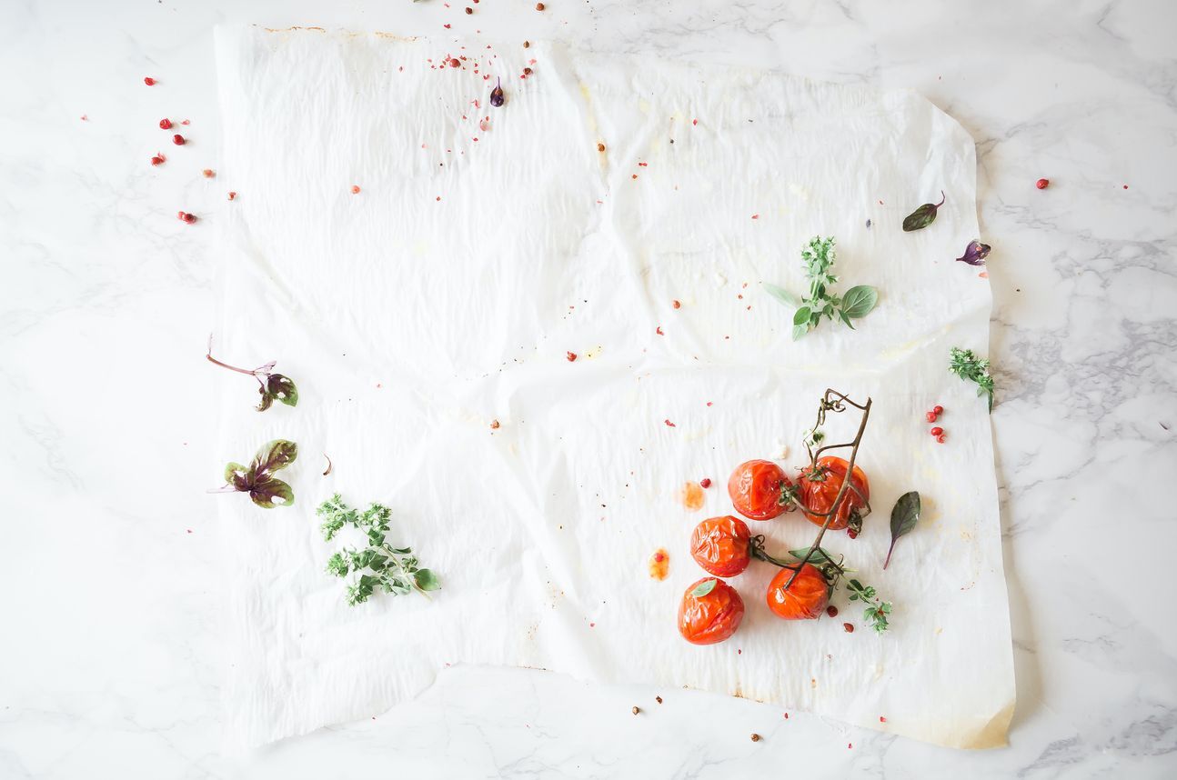 Kleine Tomaten und Kräuter auf weißem Untergrund.