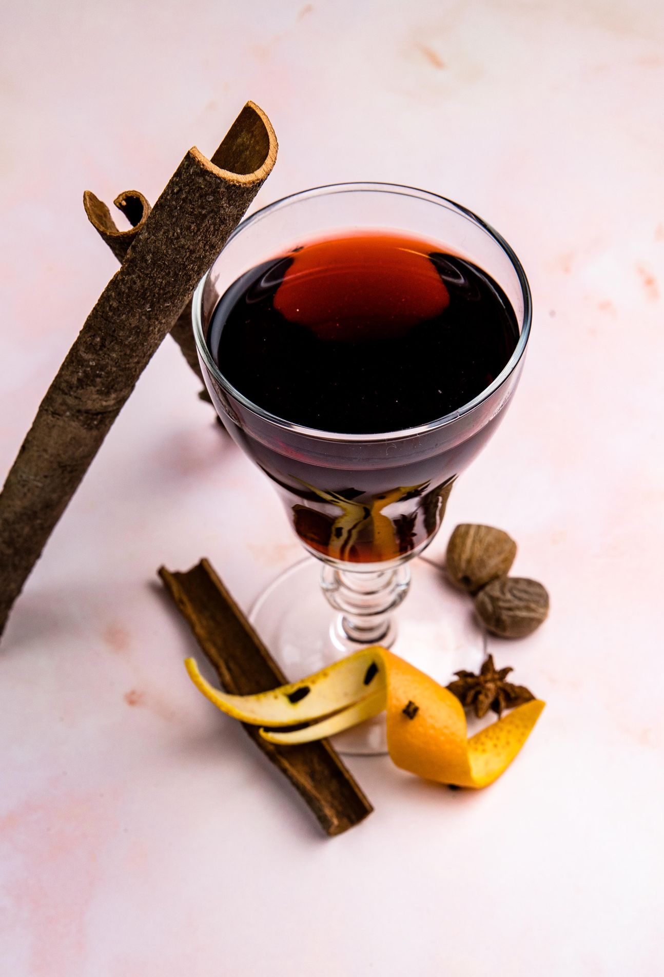 Ein Glas mit einem roten Getränk, daneben Zimmtstangen und Orangenscheibe