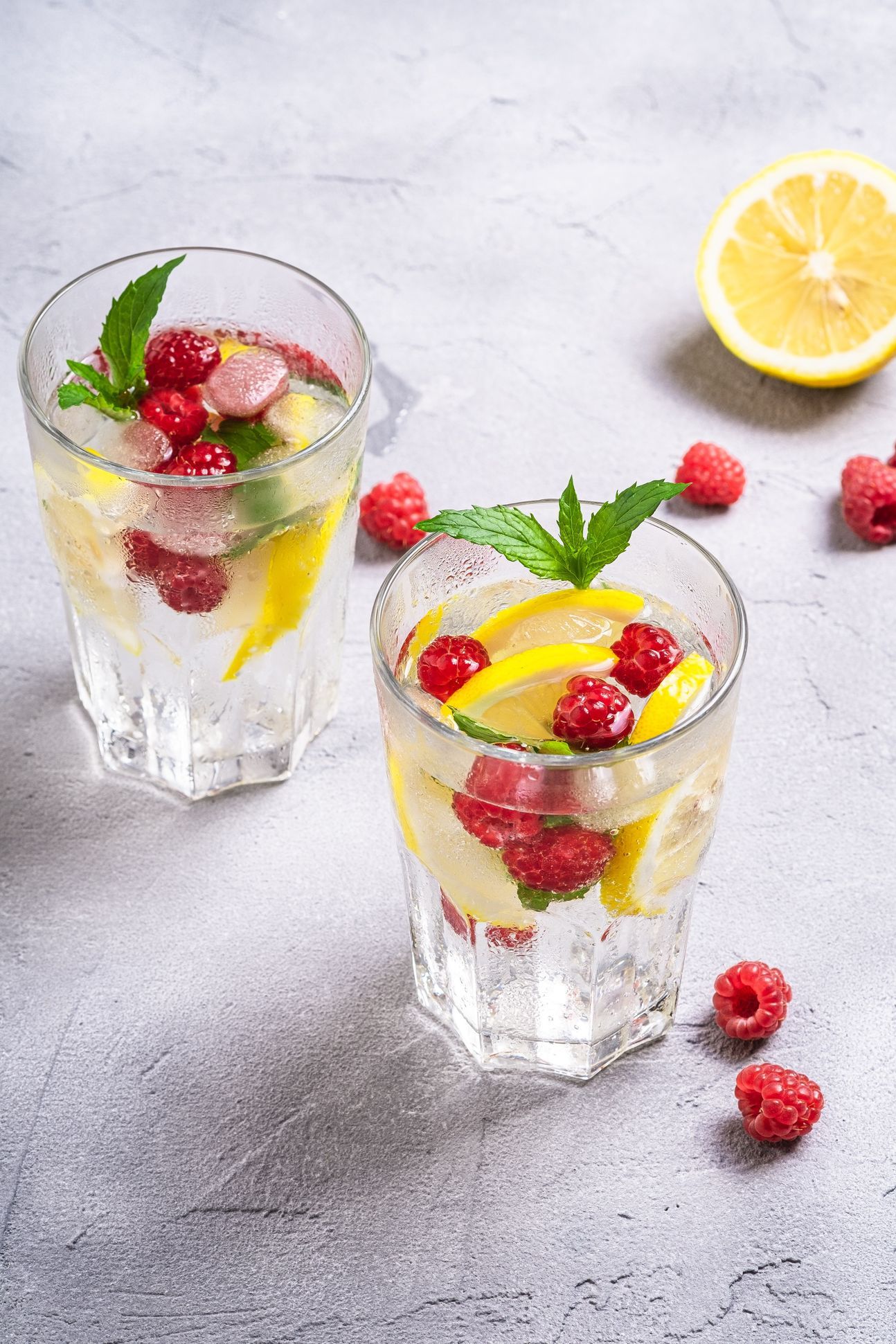 3 Gläser, gefüllt, dekoriert mit Himbeeren und Zitronen, sowie Minzblättchen