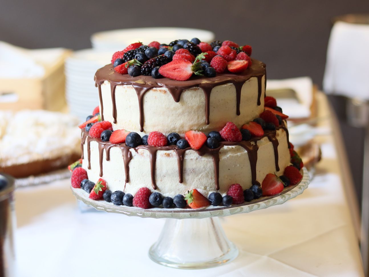 2-stöckige Torte, die mit Quark eingestrichen ist und mit fließender Schokolade und frischen Beeren dekoriert.