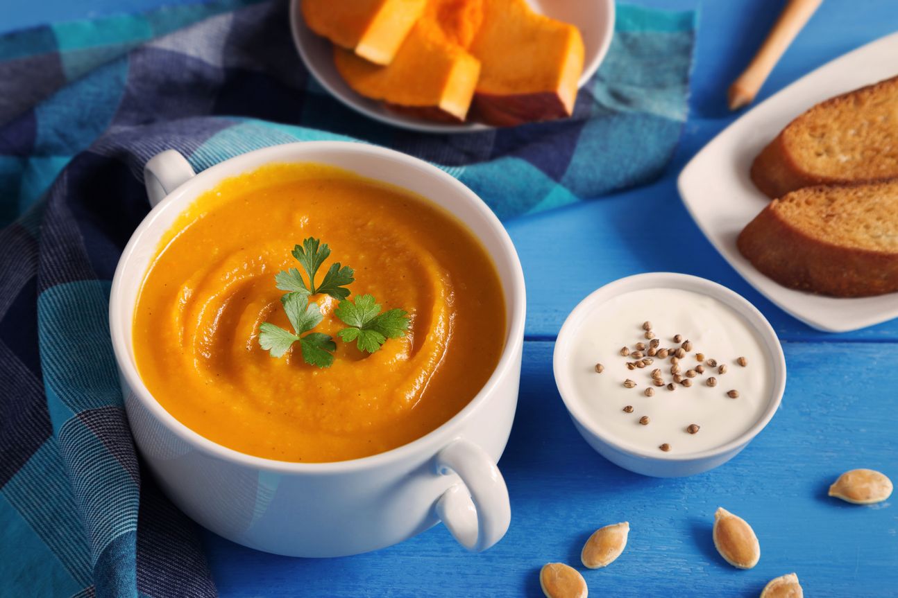 Suppentasse, gefüllt mit Suppe, auf einem blauen Tuch angerichtet.