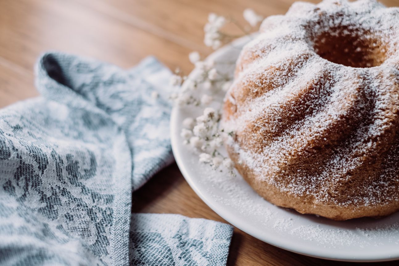 Kuchen auf weißem Teller in Napfkuchenform, mit Tuch dekoriert.