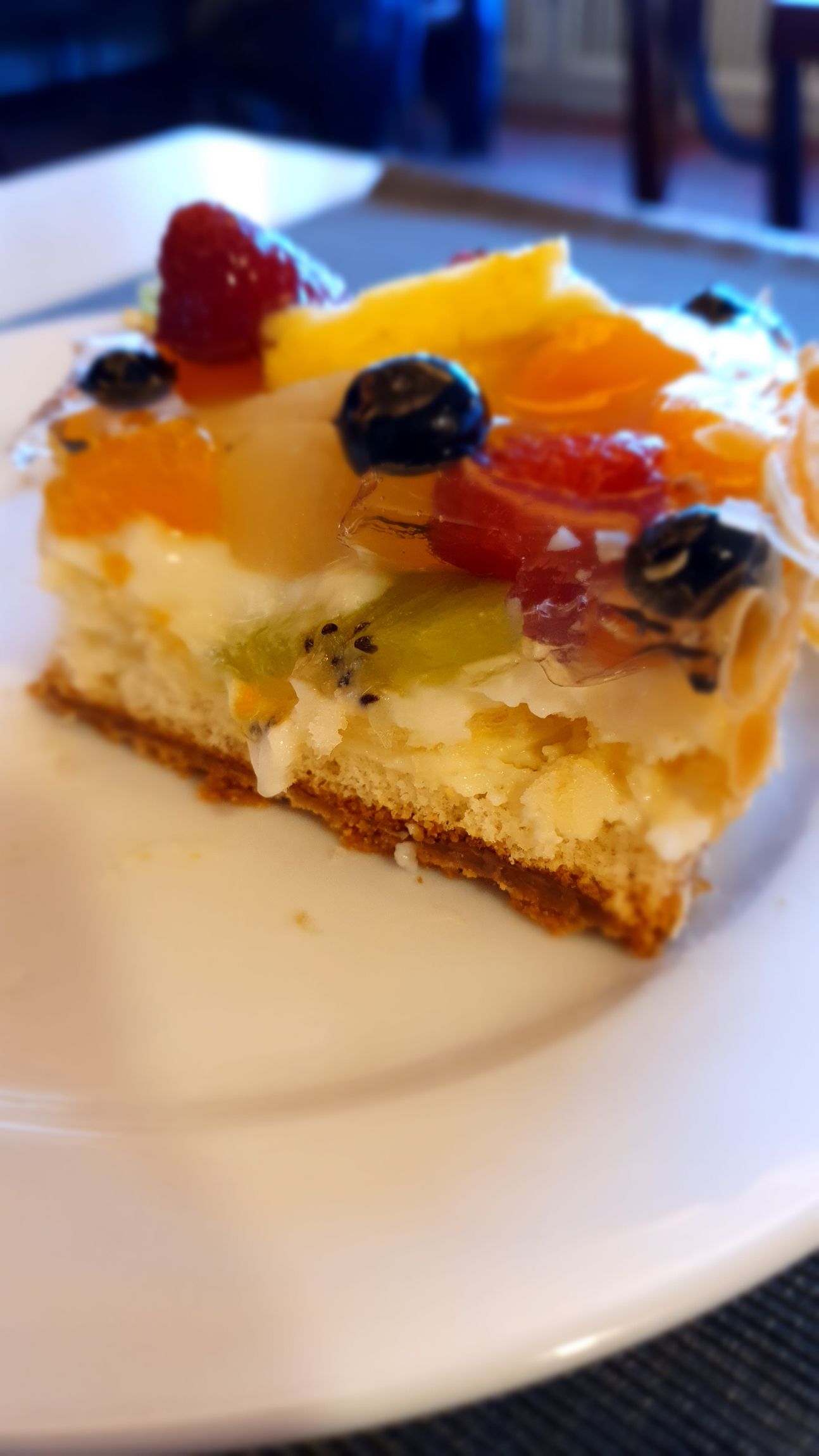 Ein Stück Obstkuchen mit verschiedenen Früchten auf einem Teller angerichtet.