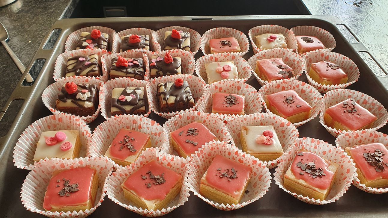 2 verschiedene Petits Fours auf einem großen Blech, bereits fertig dekoriert, einmal mit Schokolade, einmal mit rosa Zuckerguss.