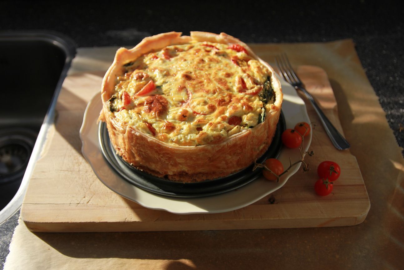 Eine ganze Quiche, angerichtet auf einem Holzbrett.