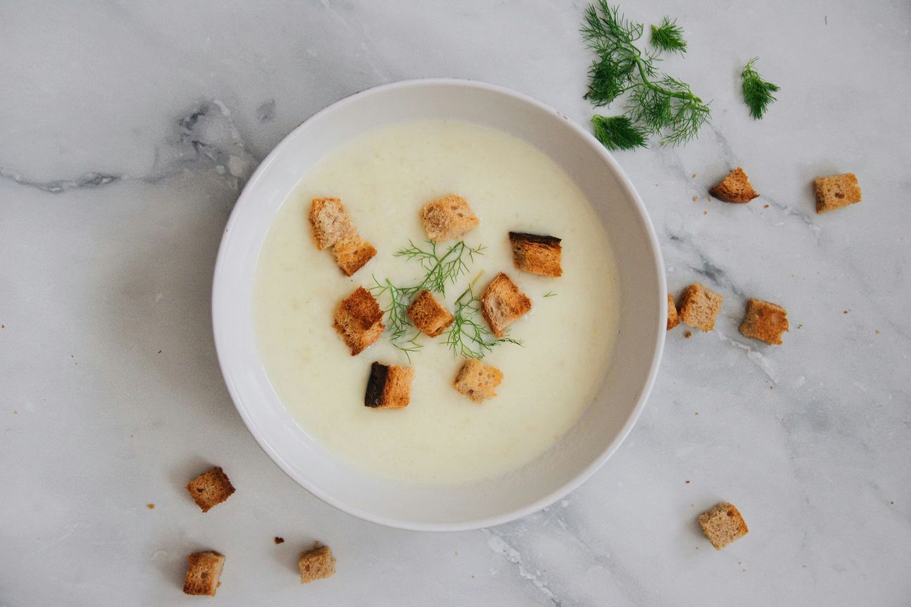 helle Suppe im Suppenteller mit kleinen Brotwürfeln